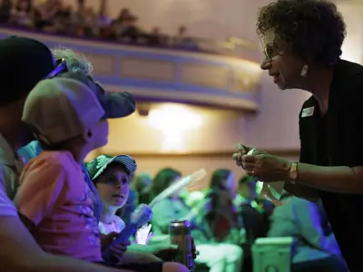 A staff member engages with children in the audience at a live performance in the Orillia Opera House, with colourful stage lighting and a lively atmosphere.