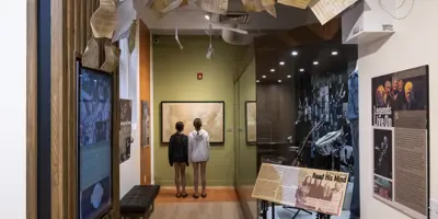 Visitors walk through an interactive museum exhibit in Orillia featuring music displays, instruments, and hanging sheet music honouring Gordon Lightfoot.