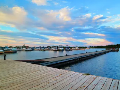 Wooden dock leading into the Port of Orillia marina with boats moored along calm water under a soft, colourful sunset sky.