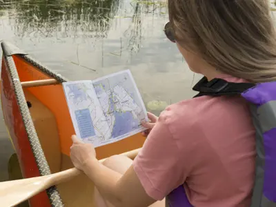 A person wearing a life jacket sits in a canoe on calm water while looking at a map of the Orillia and Lake Couchiching area.