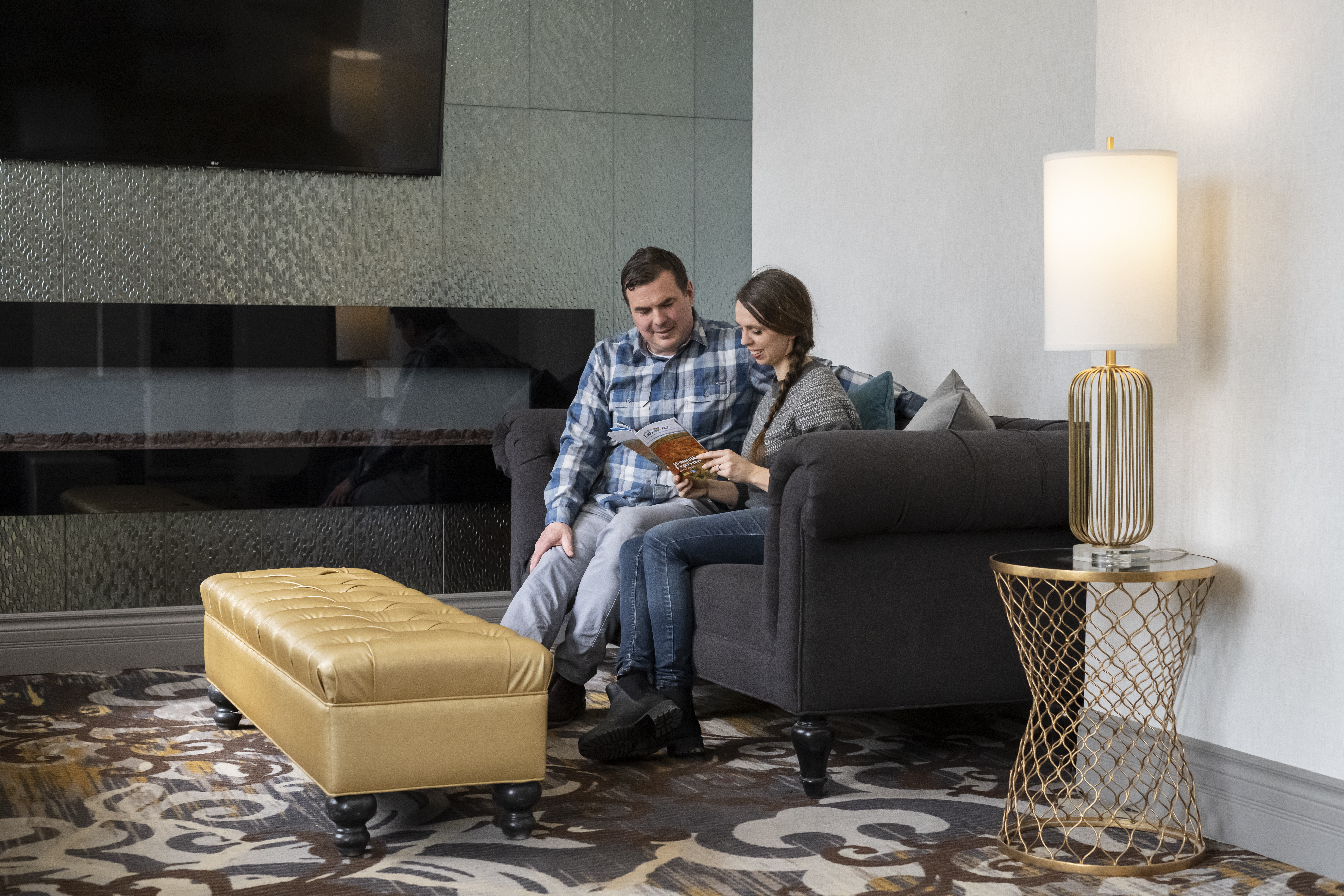 A couple sits on a comfortable sofa in a stylish hotel lounge in Orillia, reading together beside a fireplace with warm lighting and modern décor.