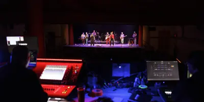 View from the sound booth of a live performance on stage at the Orillia Opera House, with musicians under stage lights and audio equipment in the foreground.
