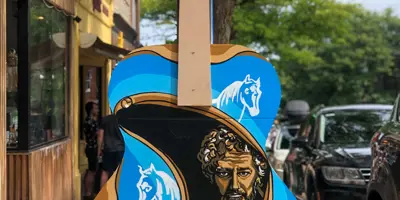 Colourfully painted guitar sculpture featuring a portrait and horse motifs displayed on a sidewalk in downtown Orillia, part of a public art installation.