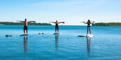 Three people stand on paddleboards on Lake Couchiching in Orillia, holding paddles and enjoying calm blue water under a clear sky.