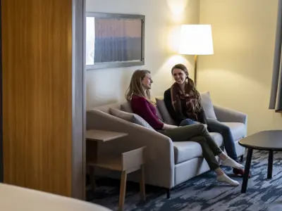 Two women sit and chat on a comfortable sofa inside a cozy hotel room in Orillia, with warm lighting, modern furnishings, and a welcoming atmosphere.