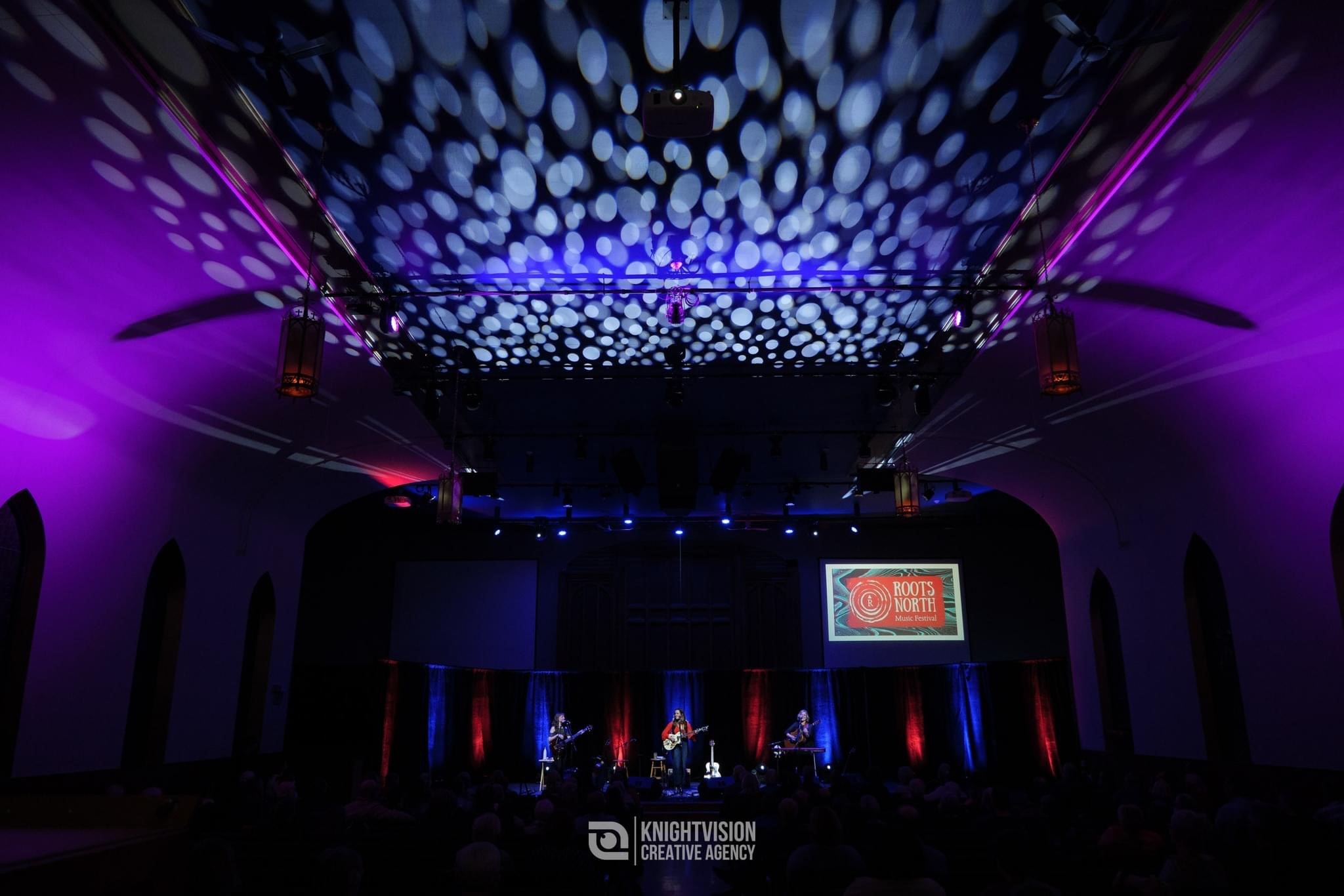 Live performance during the Roots North Music Festival at St. Paul’s Centre in Orillia, with vibrant stage lighting and patterned projections across the ceiling.