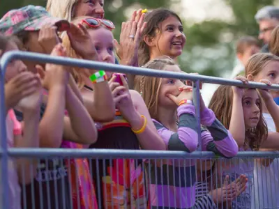 Audiences of all ages excitedly watching a stage from behind an event barricade